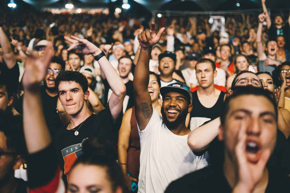 Large crowd at a live music event festival with their hands in the air whilst watching a performer